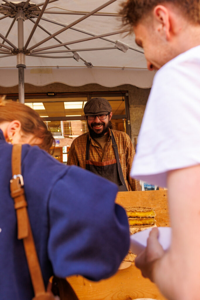 Fromager riant avec des clients au marché de la vieille ville à Annecy